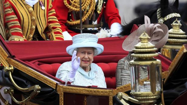 Königin Elisabeth II. winkt aus einer Kutsche.
