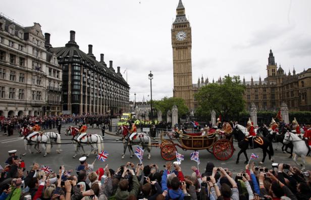 Eine Pferdekutsche fährt vor dem Big Ben in London, während Menschen am Straßenrand jubeln.