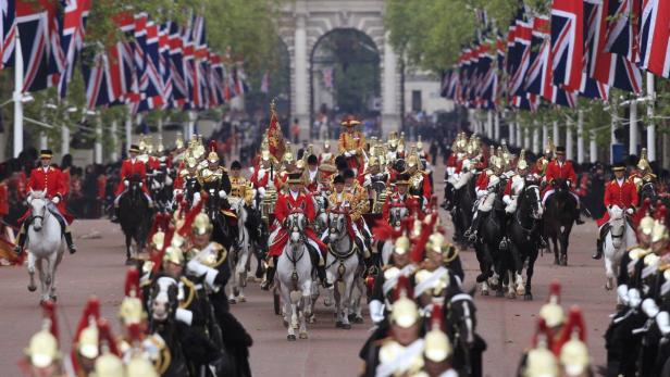 Eine Parade von berittenen Soldaten in roten Uniformen unter britischen Flaggen.