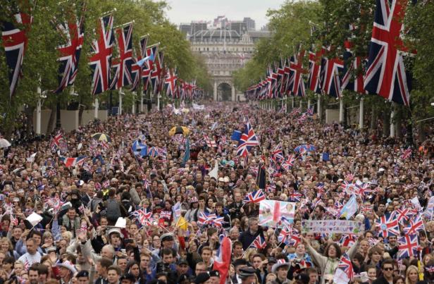 Eine große Menschenmenge mit Union-Jack-Flaggen säumt eine von britischen Flaggen gesäumte Straße in London.
