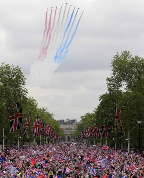 Eine Menschenmenge mit Union Jacks beobachtet eine Flugstaffel am Himmel.