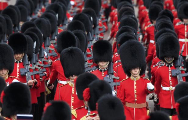 Eine Reihe von britischen Gardesoldaten in roten Uniformen und Bärenfellmützen marschiert auf einer Parade.