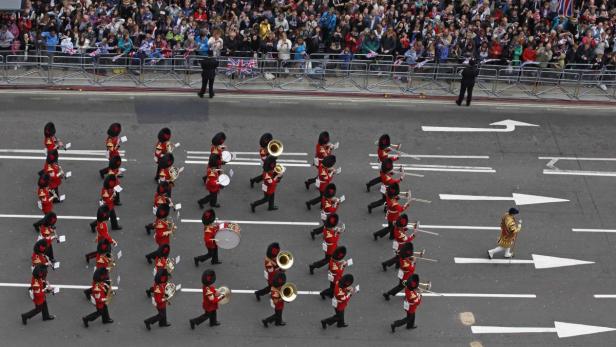 Eine Militärkapelle marschiert auf einer Straße, während Zuschauer hinter Absperrungen stehen.