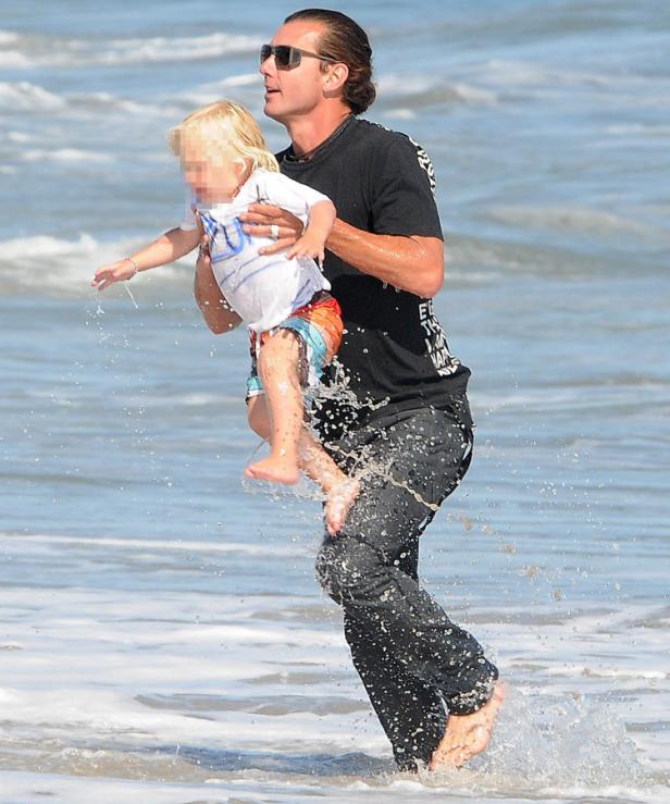 Ein Mann trägt ein Kind am Strand durch das Wasser.