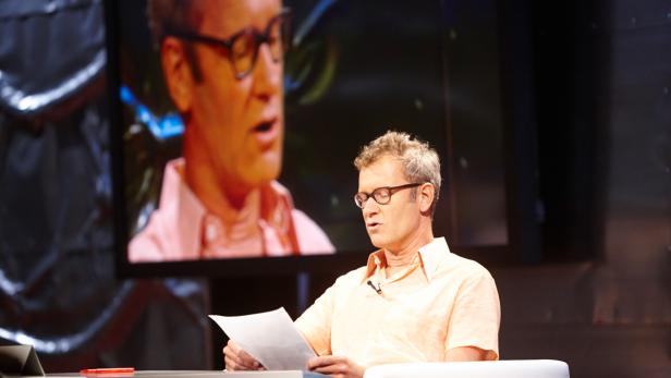 Ein Mann mit Brille liest ein Dokument vor einem Bildschirm, der sein Gesicht zeigt.