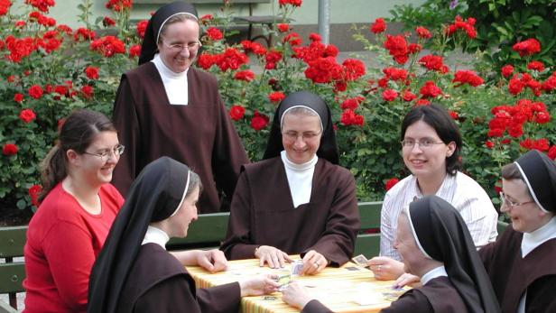 Eine Gruppe von Nonnen und Frauen spielt Karten vor einem Rosenbeet.