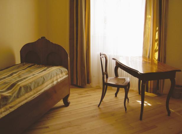 Ein Schlafzimmer mit einem Bett, einem Schreibtisch und einem Stuhl bei Tageslicht.