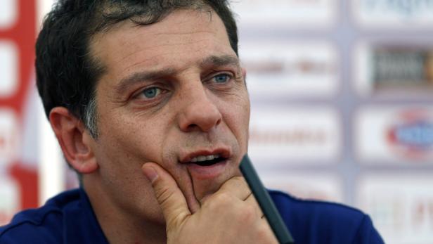 Ein Mann mit blauem Hemd spricht und hält seine Hand ans Kinn.