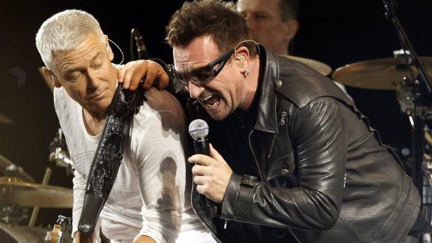 Bono von U2 singt mit Sonnenbrille in ein Mikrofon, während The Edge Gitarre spielt.