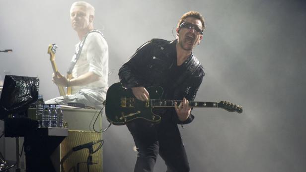 Bono von U2 spielt Gitarre auf der Bühne.