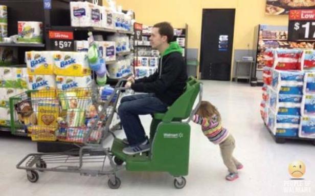 Ein Mann fährt in einem Walmart auf einem motorisierten Einkaufswagen, während ein kleines Kind ihn schiebt.