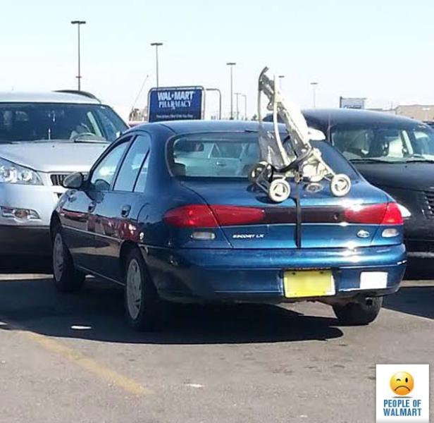 Ein Kinderwagen ist mit Spanngurten an der Rückseite eines blauen Autos auf einem Parkplatz befestigt.