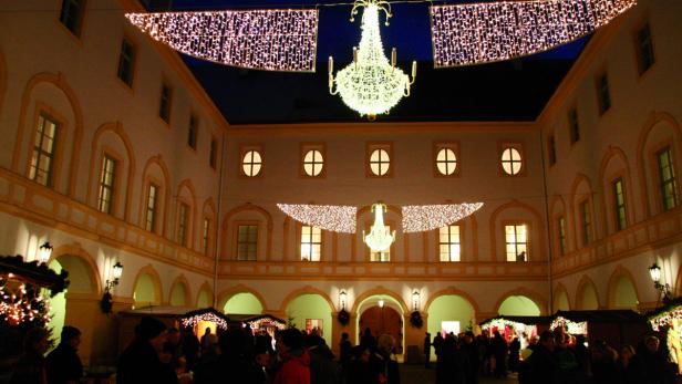 Ein Weihnachtsmarkt im Innenhof eines Schlosses mit festlicher Beleuchtung.