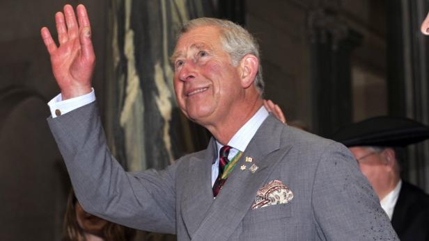 König Charles III. winkt in einem grauen Anzug.