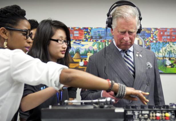 Prinz Charles legt mit Kopfhörern und unter Anleitung an einem DJ-Pult auf.