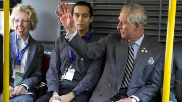 Prinz Charles winkt, während er mit anderen Personen in einem Bus sitzt.