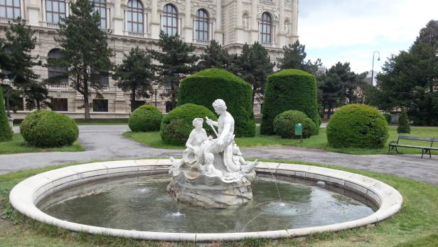 Ein Brunnen mit einer Skulptur im Park vor einem Gebäude in Wien.