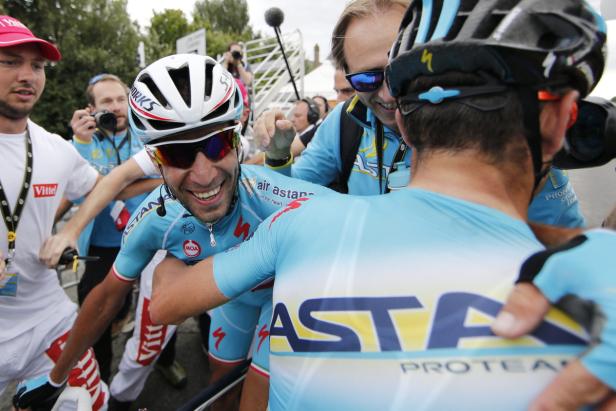Vincenzo Nibali wird von seinen Teamkollegen gefeiert. Ein Radrennfahrer im blauen Trikot von Astana umarmt einen Teamkollegen und lächelt.