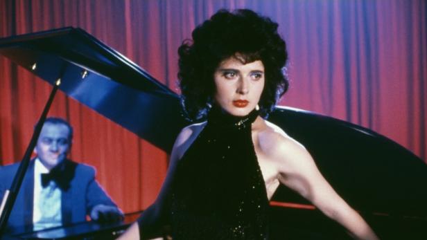 Eine Frau in einem schwarzen Kleid steht vor einem Klavier, während ein Mann es spielt.