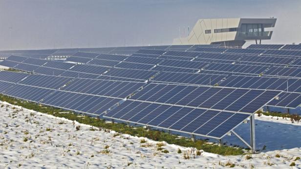 Ein Solarpark im Winter mit einem modernen Gebäude im Hintergrund.