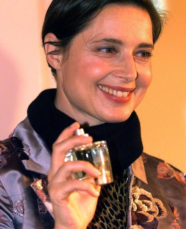 Eine lächelnde Frau hält einen Parfümflakon in der Hand.