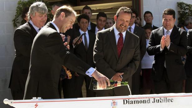 Ein Mann zerschmettert eine Champagnerflasche an einem Boot mit der Aufschrift „Diamond Jubilee“.