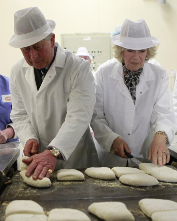 König Charles und Königin Camilla in Arbeitskleidung beim Formen von Teiglingen.