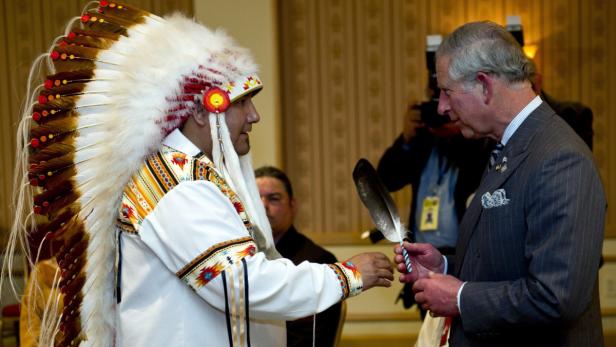Ein Mann mit traditioneller Kopfbedeckung überreicht Prinz Charles eine Feder.