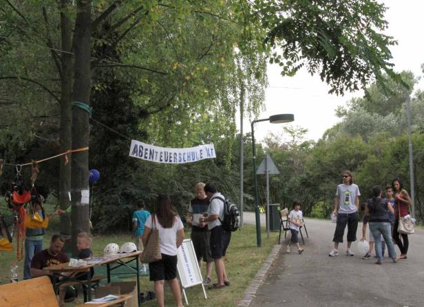 Eine Gruppe von Menschen versammelt sich vor einem Banner mit der Aufschrift „Abenteuerschule AT“.