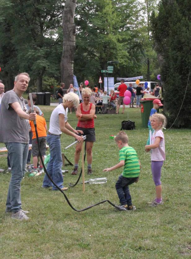 Eine Gruppe von Menschen, darunter Kinder, spielt mit einer Wasserrakete im Park.