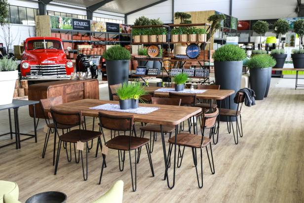 Ein Verkaufsraum mit Holztischen, Stühlen und Dekoration, im Hintergrund ein roter Oldtimer-Truck.