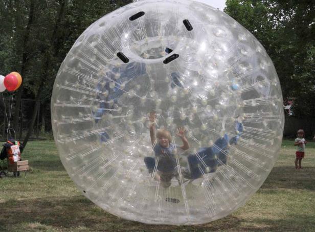 Ein Kind spielt in einer grossen, durchsichtigen Zorb-Kugel auf einer Wiese.