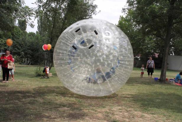 Eine Person befindet sich in einer grossen, transparenten Zorb-Kugel auf einer Wiese.