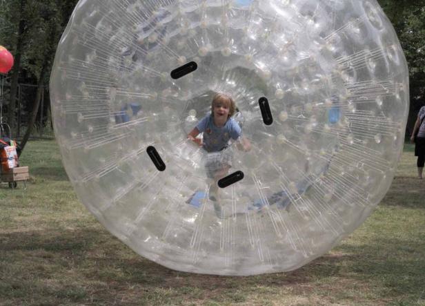 Ein Kind spielt in einer grossen, durchsichtigen Zorb-Kugel auf einer Wiese.