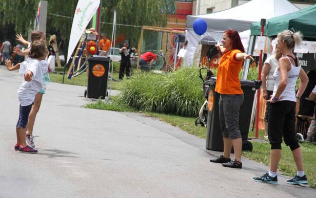 Zwei Mädchen ahmen die Bewegungen einer Frau an einem Stand im Freien nach.