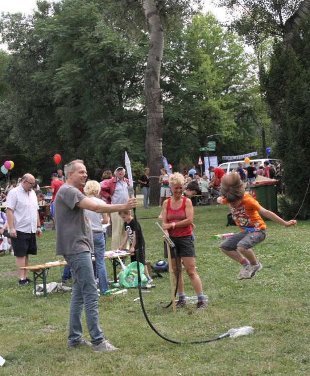 Ein Junge springt über ein Spielzeug, das von einem Mann und einer Frau im Park bedient wird.