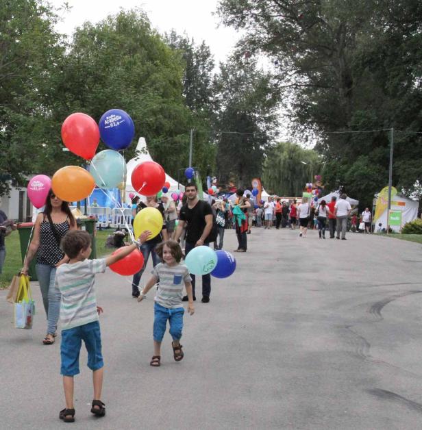 Zwei Kinder laufen mit Luftballons auf einer belebten Straße entlang.