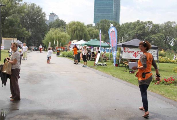 Eine Frau geht an einem sonnigen Tag durch einen Park mit Tanzschulständen.