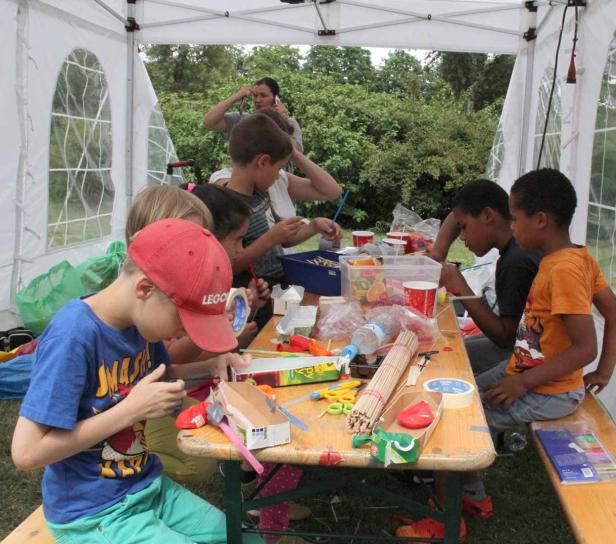 Kinder basteln gemeinsam an einem Tisch in einem Zelt.