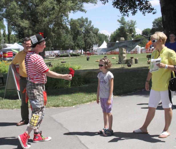 Ein Clown mit roter Nase und gestreiftem Hemd unterhält ein junges Mädchen.