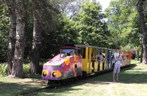 Ein bunter Zug fährt durch einen Park, während ein Mann daneben steht.