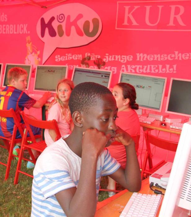 Kinder sitzen an Computern unter einem Kiku-Banner.