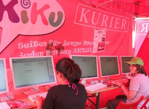 Zwei Personen sitzen vor Computern unter einem Stand von „KiKu Kurier“.