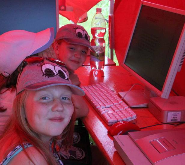 Zwei Mädchen mit lustigen Mützen sitzen an einem Computer in einem roten Zelt.