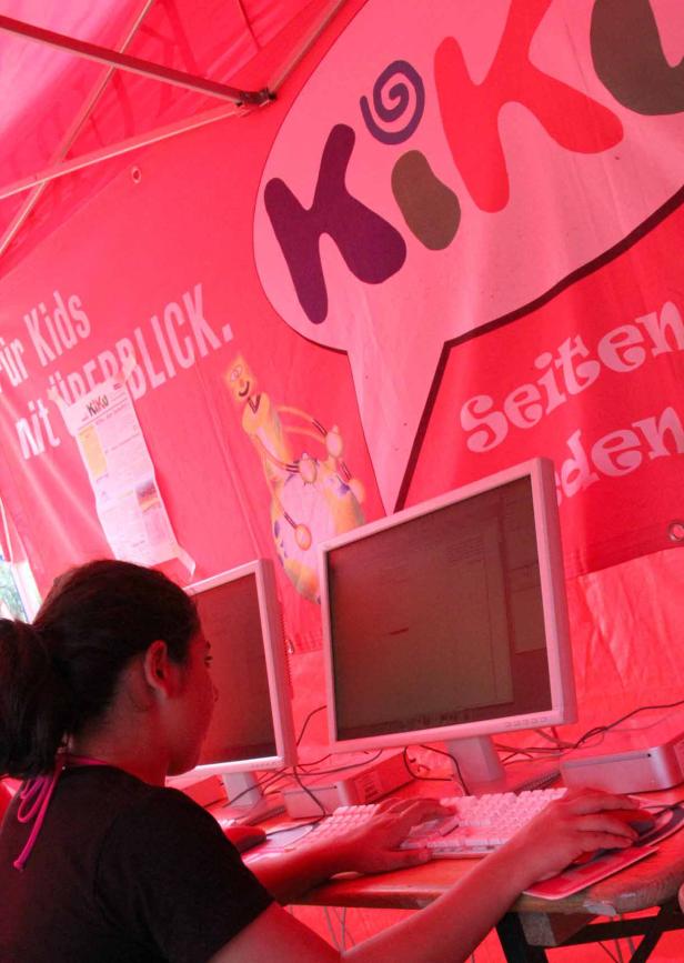 Eine junge Frau sitzt an einem Stand mit Computern und dem Logo von „KiKo“.