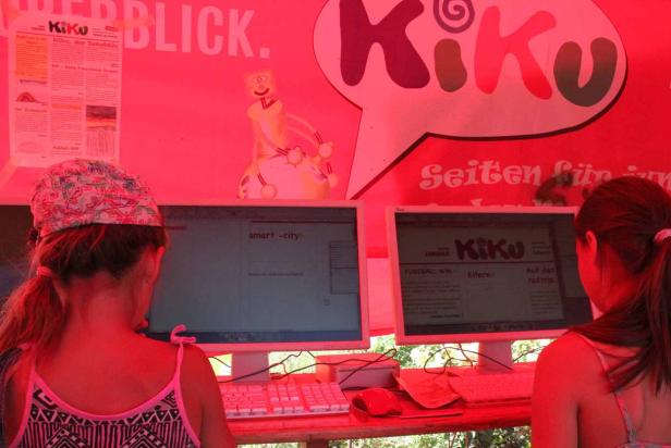 Zwei Mädchen sitzen vor Computern mit der Aufschrift „Kiku“ und „smart-city“.