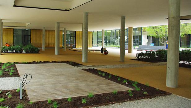 Ein Innenhof mit gelbem Bodenbelag, Betonpfeilern und neu angelegten Grünflächen.