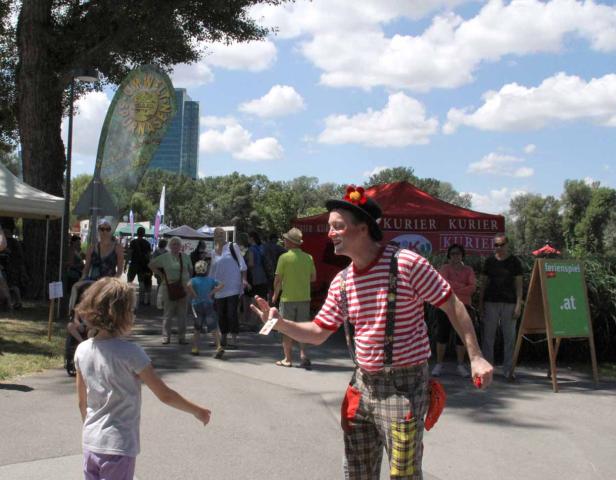 Ein Clown mit rot-weiß gestreiftem Hemd unterhält ein Kind auf einer Veranstaltung.