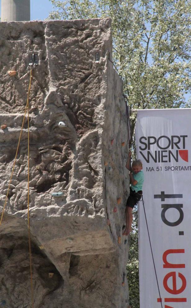 Ein Kind klettert an einer Kletterwand neben einem „Sport Wien“-Banner.