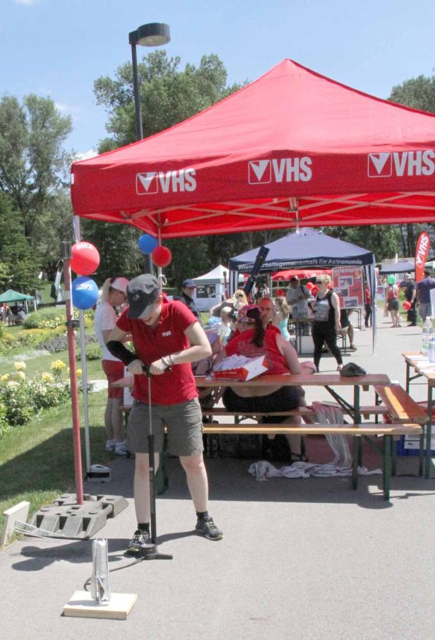 Eine Frau pumpt unter einem roten VHS-Zelt eine Rakete auf einem öffentlichen Platz auf.